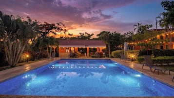 Ein Swimmingpool mit Liegestühlen, ein Gebäude mit roten Ziegeldach und Lichterketten.
