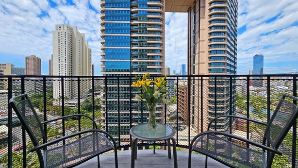 Un balcone con due sedie e un tavolo, affacciato su un panorama urbano con edifici alti.