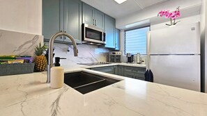 A modern kitchen with a stainless steel sink, a microwave, a built-in oven, and a refrigerator. - Free Parking, Beach Gear Included, 2BR 1BA in Waikiki (Waikiki)