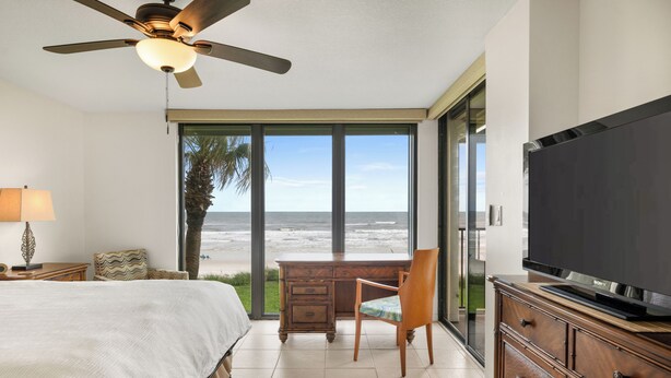 Ein Schlafzimmer mit Bett, Schreibtisch, Stuhl, Fernseher und Meerblick.