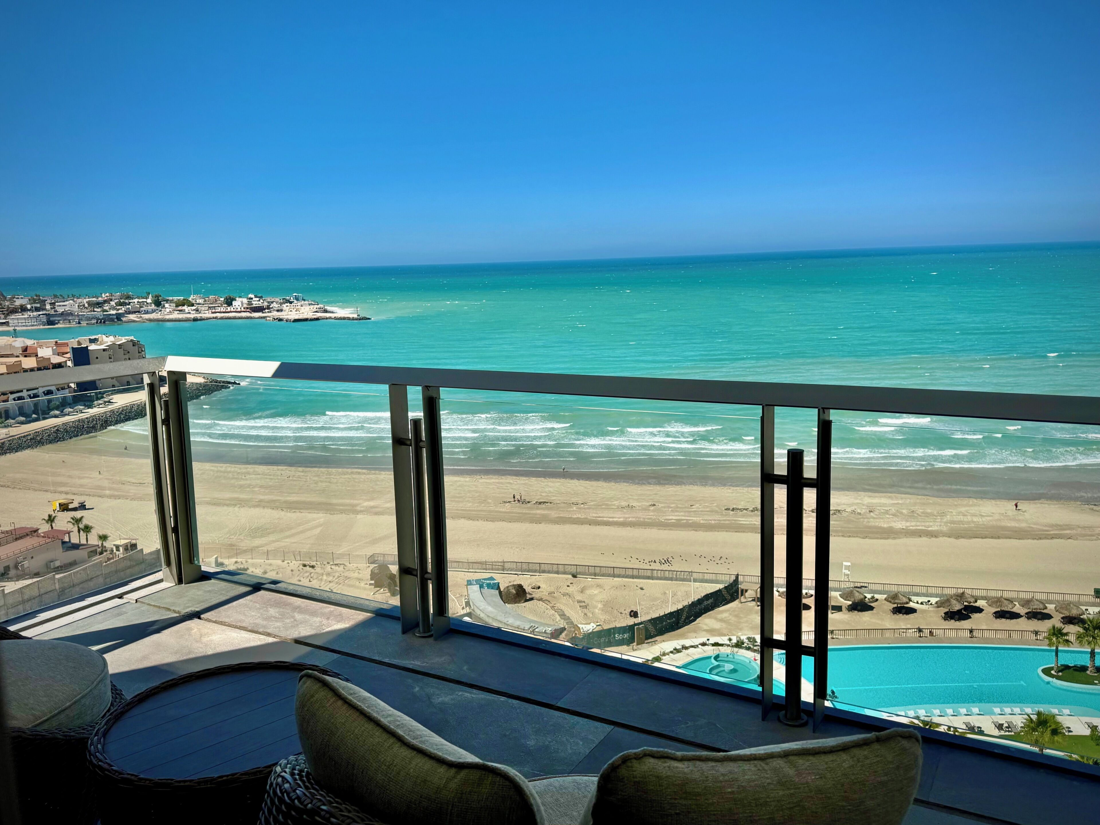 A balcony with a view of the beach, a pool, and a distant pier.