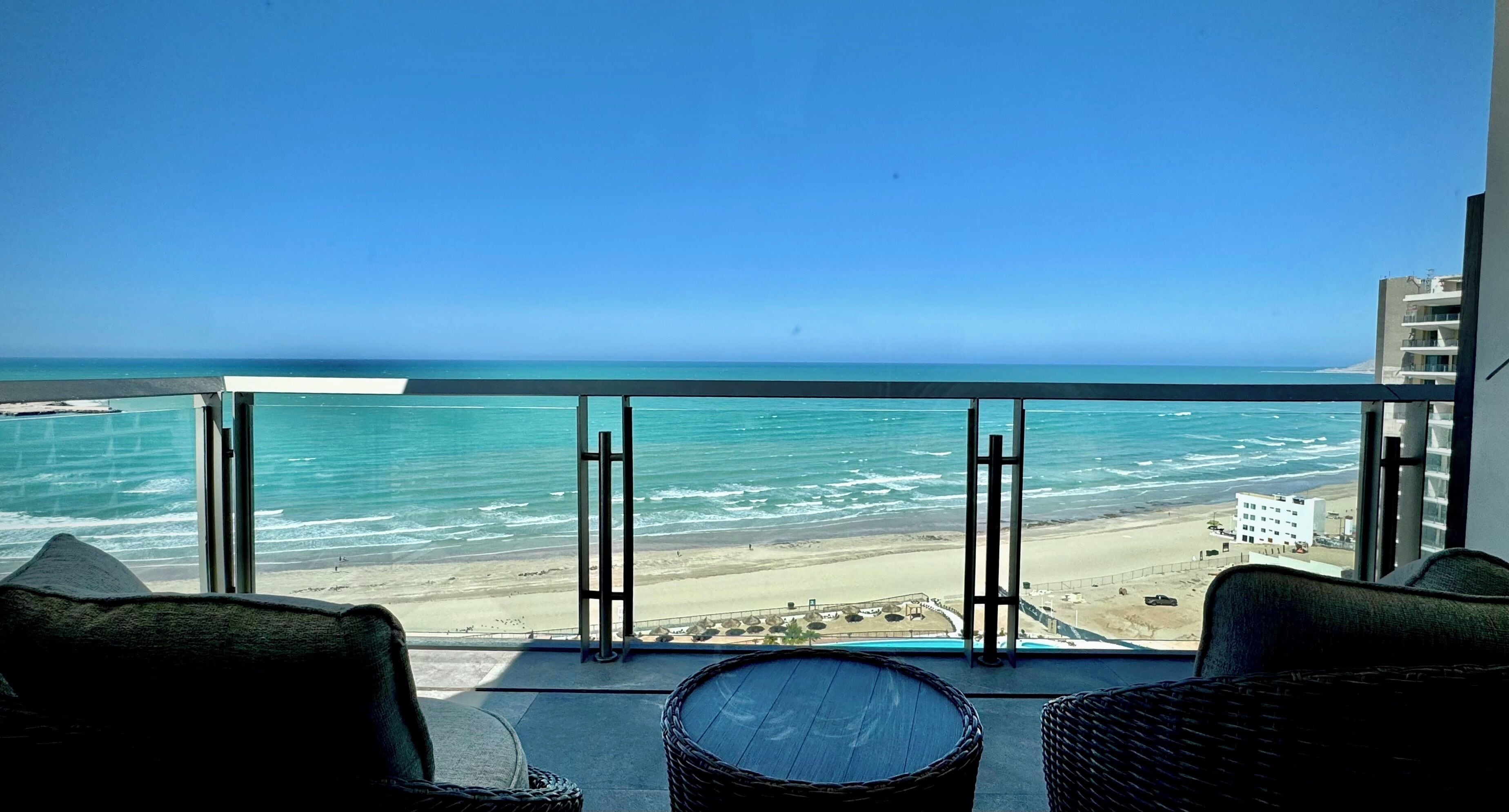 Ein Balkon mit Korbmöbeln, der Blick auf einen Strand und das Meer bietet.