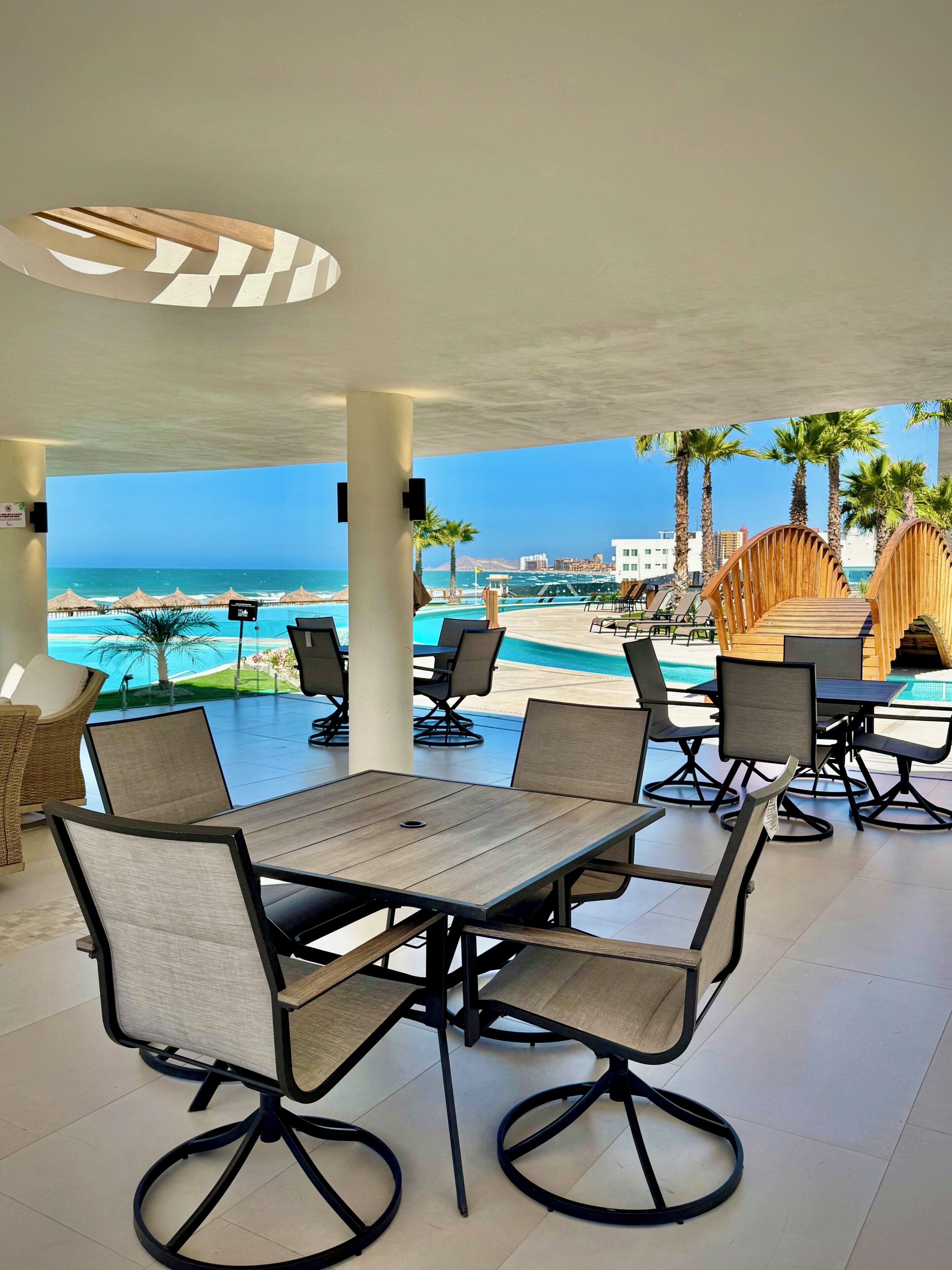 Un espace extérieur aménagé, abrité et doté de tables et de chaises, offrant une vue sur une piscine et une plage.
