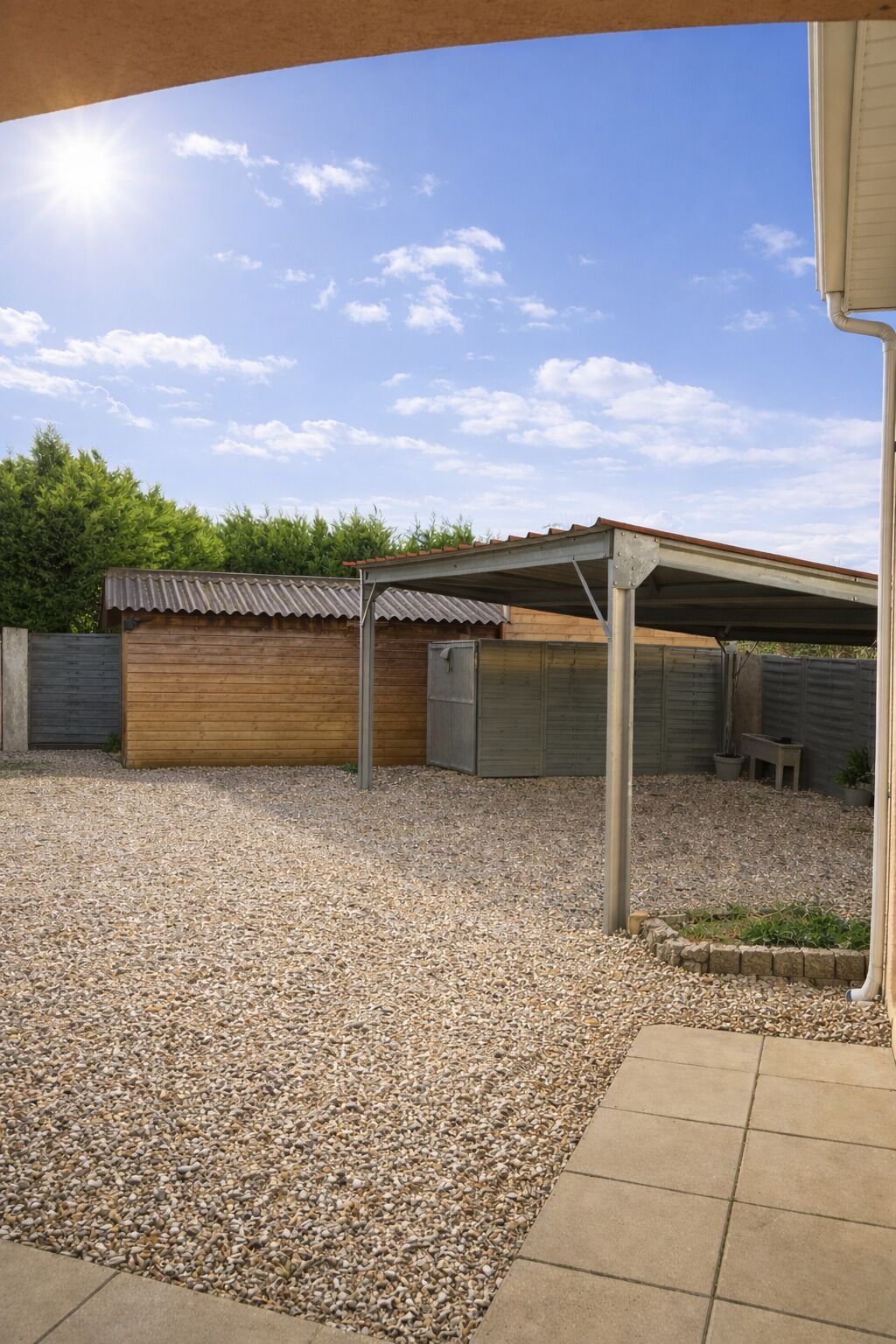 A covered outdoor area with a gravel ground, a wooden structure, and a metal roof.