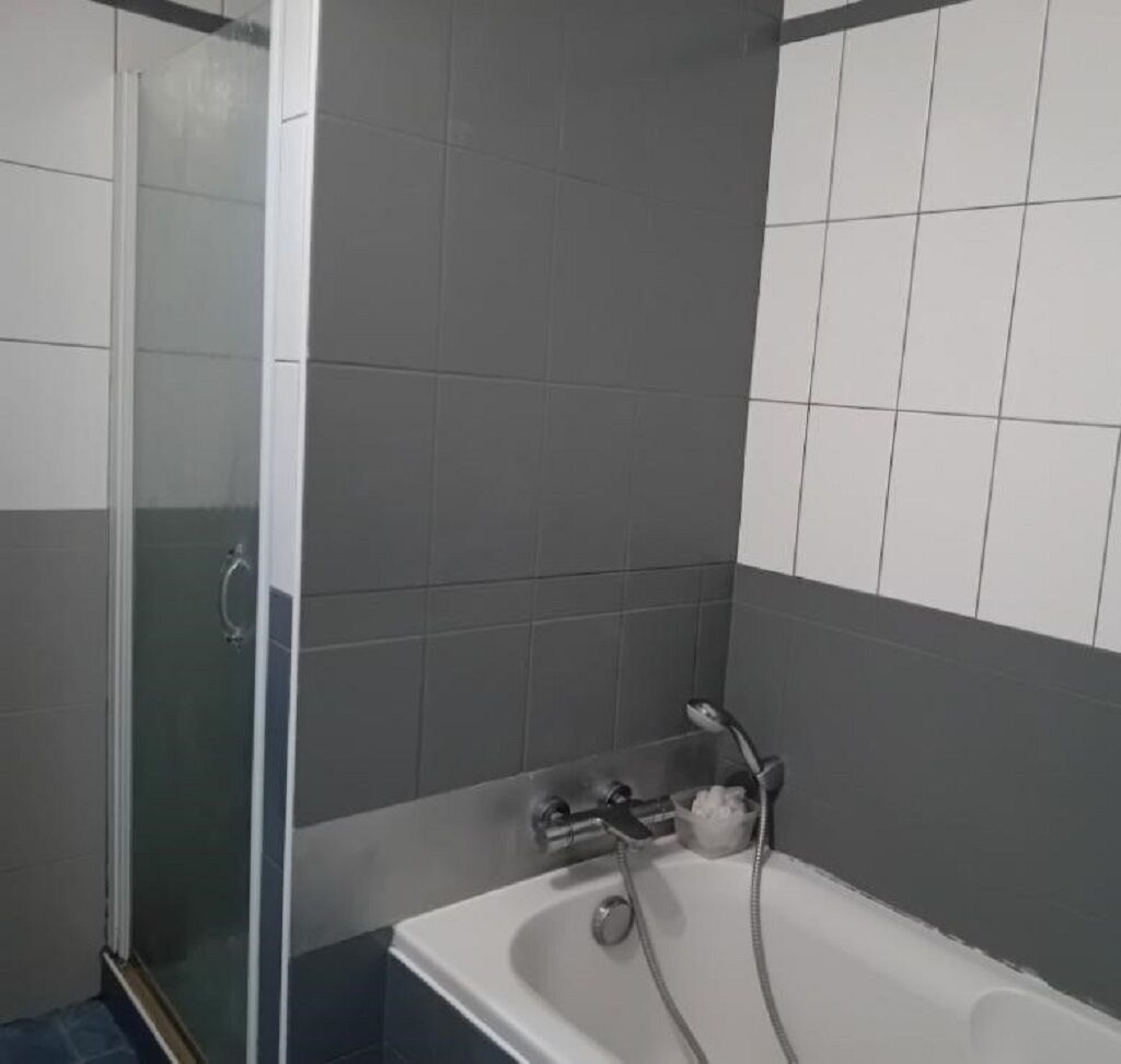 A bathroom with a glass shower enclosure, a bathtub, and tiled walls.