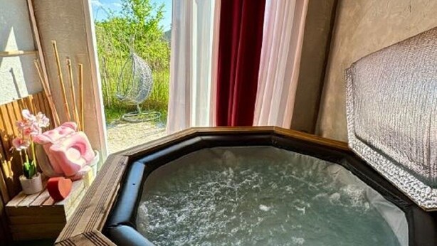Een bubbelbad in een kamer met een houten plafond, een raam met gordijnen en uitzicht op groen buiten.