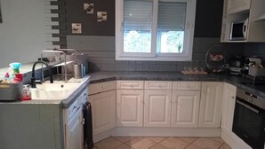 Een keuken met witte kastjes, een raam, een magnetron en een spoelbak.
