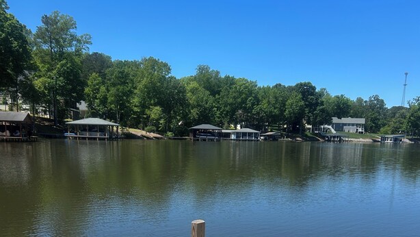 A wooden dock with two red Adirondack chairs facing a calm lake, surrounded by trees and buildings. - Premium Waterfront 5BR/3.5BA. Boat House, Kayaks, Lillypad, Wheelchair-friendly (Littleton)
