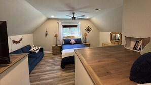 A bedroom with a bed, a desk, a chair, a ceiling fan, a window with curtains, a wall-mounted TV, and a bookshelf. - Premium Waterfront 5BR/3.5BA. Boat House, Kayaks, Lillypad, Wheelchair-friendly (Littleton)