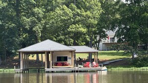 A lakeside cabin with a dock, outdoor seating, and a boat. - Premium Waterfront 5BR/3.5BA. Boat House, Kayaks, Lillypad, Wheelchair-friendly (Littleton)