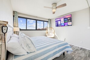 A bedroom with a bed, a ceiling fan, a TV displaying streaming services, a window, and a chair. - Family Condo: Ocean View + King Bed + Hot Tub + Pool (Myrtle Beach)