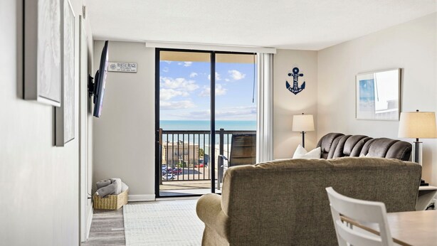 A room with a view of the beach, a leather sofa, a dining table, and a lamp. - Family Condo: Ocean View + King Bed + Hot Tub + Pool (Myrtle Beach)