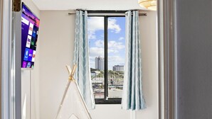 A room with a window, curtains, a TV on the wall, and a white tent-like structure. - Family Condo: Ocean View + King Bed + Hot Tub + Pool (Myrtle Beach)