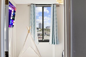 A room with a window, curtains, a TV on the wall, and a white tent-like structure. - Family Condo: Ocean View + King Bed + Hot Tub + Pool (Myrtle Beach)