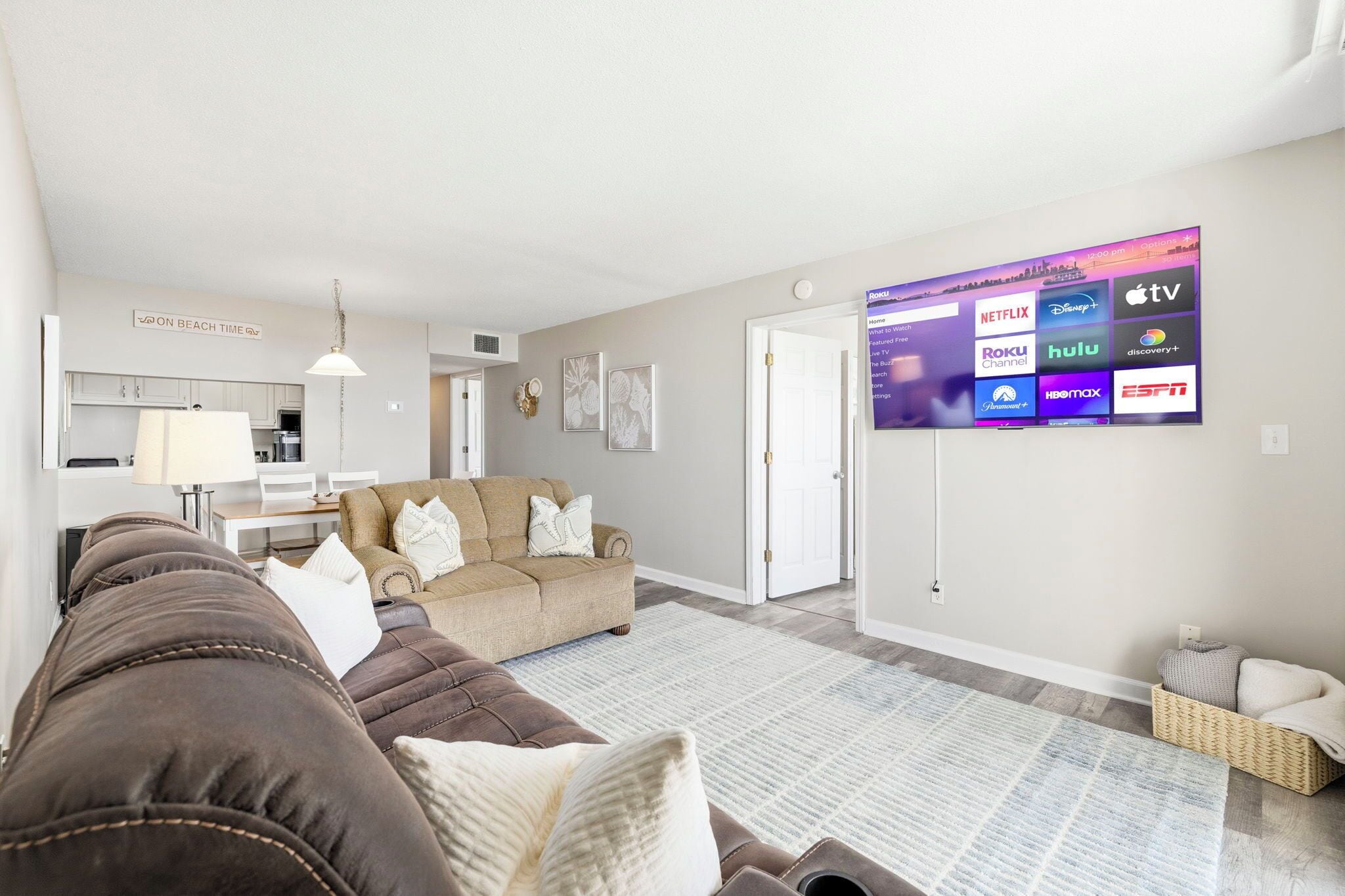 A living room with a sofa, a television displaying various streaming services, and a kitchen area in the background.