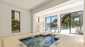 An indoor swimming pool with clear glass walls, a hot tub, and a poolside area with lounge chairs. - Family Condo: Ocean View + King Bed + Hot Tub + Pool (Myrtle Beach)
