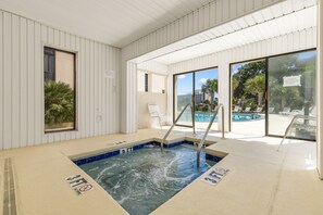 An indoor swimming pool with clear glass walls, a hot tub, and a poolside area with lounge chairs. - Family Condo: Ocean View + King Bed + Hot Tub + Pool (Myrtle Beach)
