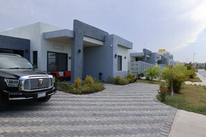 A modern building with a 'WELCOME' sign, a paved driveway, and a parked SUV. - Velvet at Paradisiac/Private Beach, Pool & Gated Luxury (Llandovery)