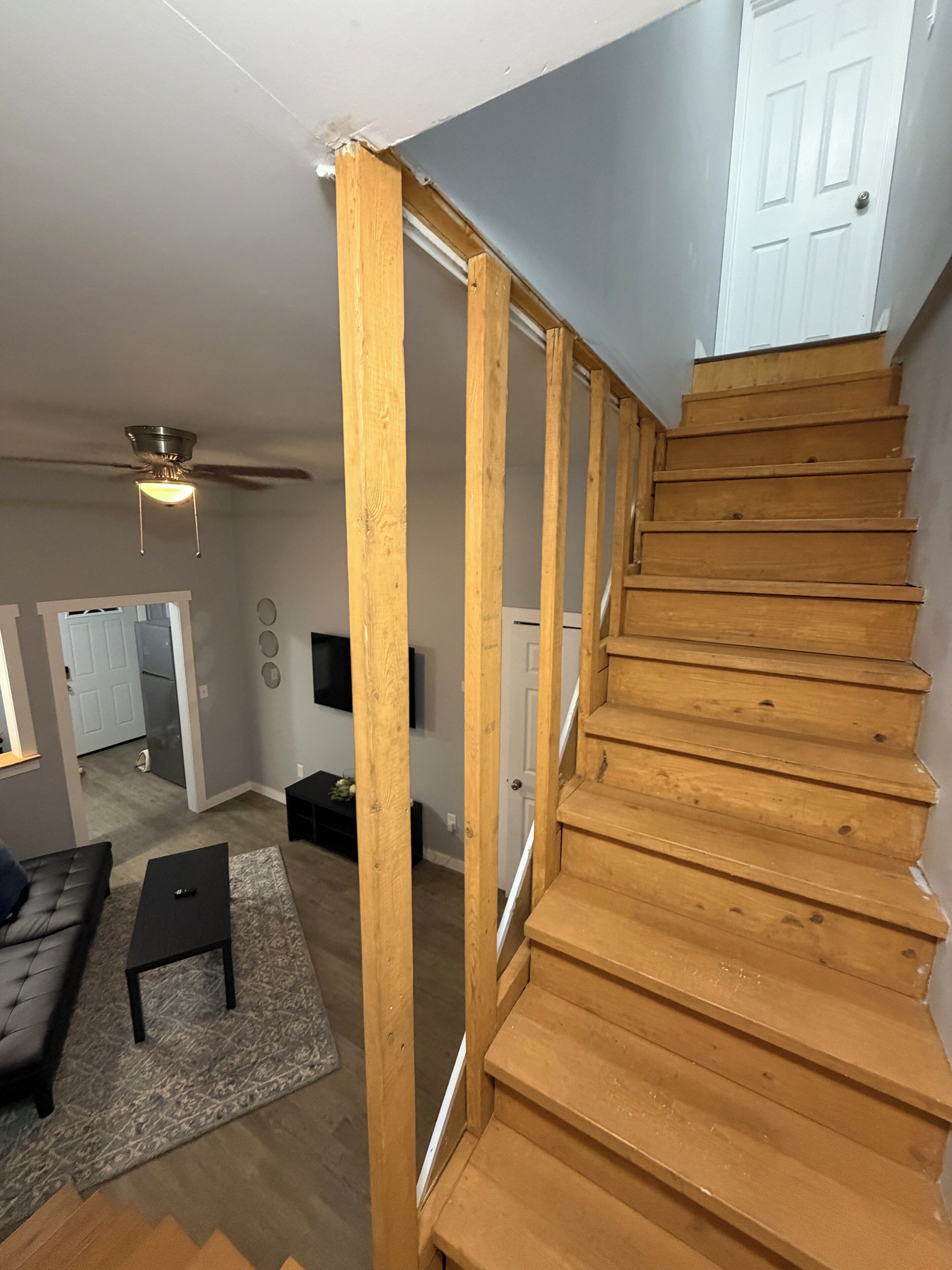 A staircase with wooden steps leading to a landing, a ceiling fan, a black leather sofa, a small table, and a patterned rug.