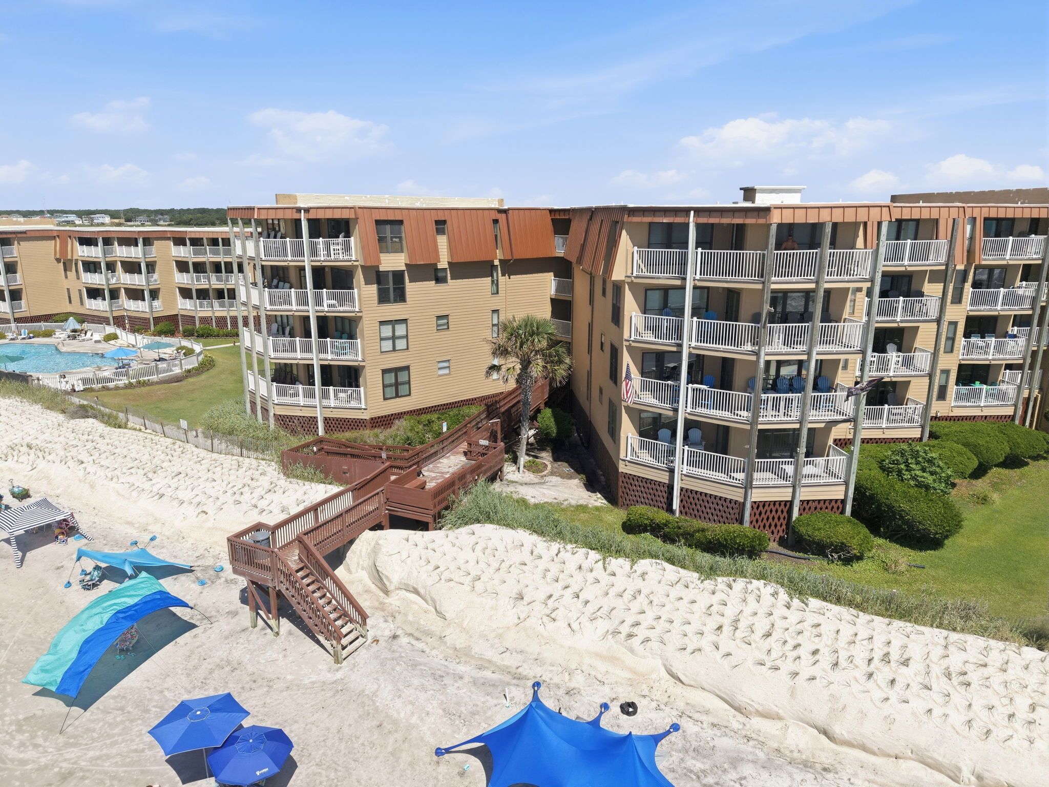 A beachfront hotel with multiple balconies, a pool, and a sandy beach area.