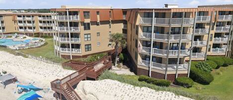 A beachfront hotel with multiple balconies, a pool, and a sandy beach area.