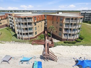Un edificio de varios pisos con balcones, un área de playa arenosa con sombrillas y una vista despejada del agua al fondo.