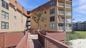 A multi-story building with balconies and a wooden walkway leading to the entrance.