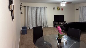 A living room with a glass table, chairs, a TV, and a ceiling fan. - Charming 2-bedroom apartment with AC in sunny Clearwater (Clearwater)