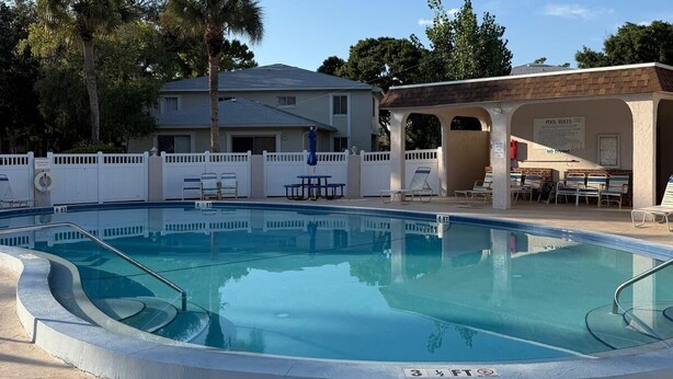 A swimming pool with a white fence, lounge chairs, and a covered area with a sign. - Charming 2-bedroom apartment with AC in sunny Clearwater (Clearwater)