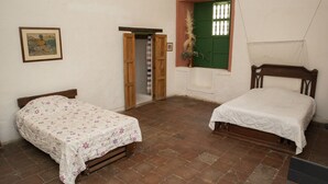 Quarto com duas camas, uma porta de madeira, uma janela com persiana verde e um quadro na parede.