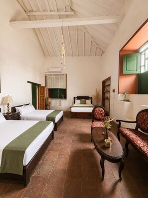Une chambre d’hôtel avec deux lits, une table, des chaises, un luminaire suspendu et une fenêtre avec un volet vert.