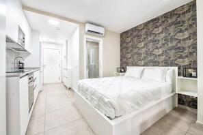 Een slaapkamer met een wit bed, een klein nachtkastje, een garderobe en een badkamer met douche en toilet.