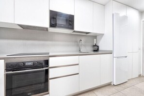 Eine moderne Küche mit weißen Schränken, einer eingebauten Mikrowelle, einem Edelstahlbackofen und einem Kühlschrank.
