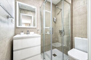 Een moderne badkamer met een douchecabine van glas, een wit wastafeltje en een toilet.