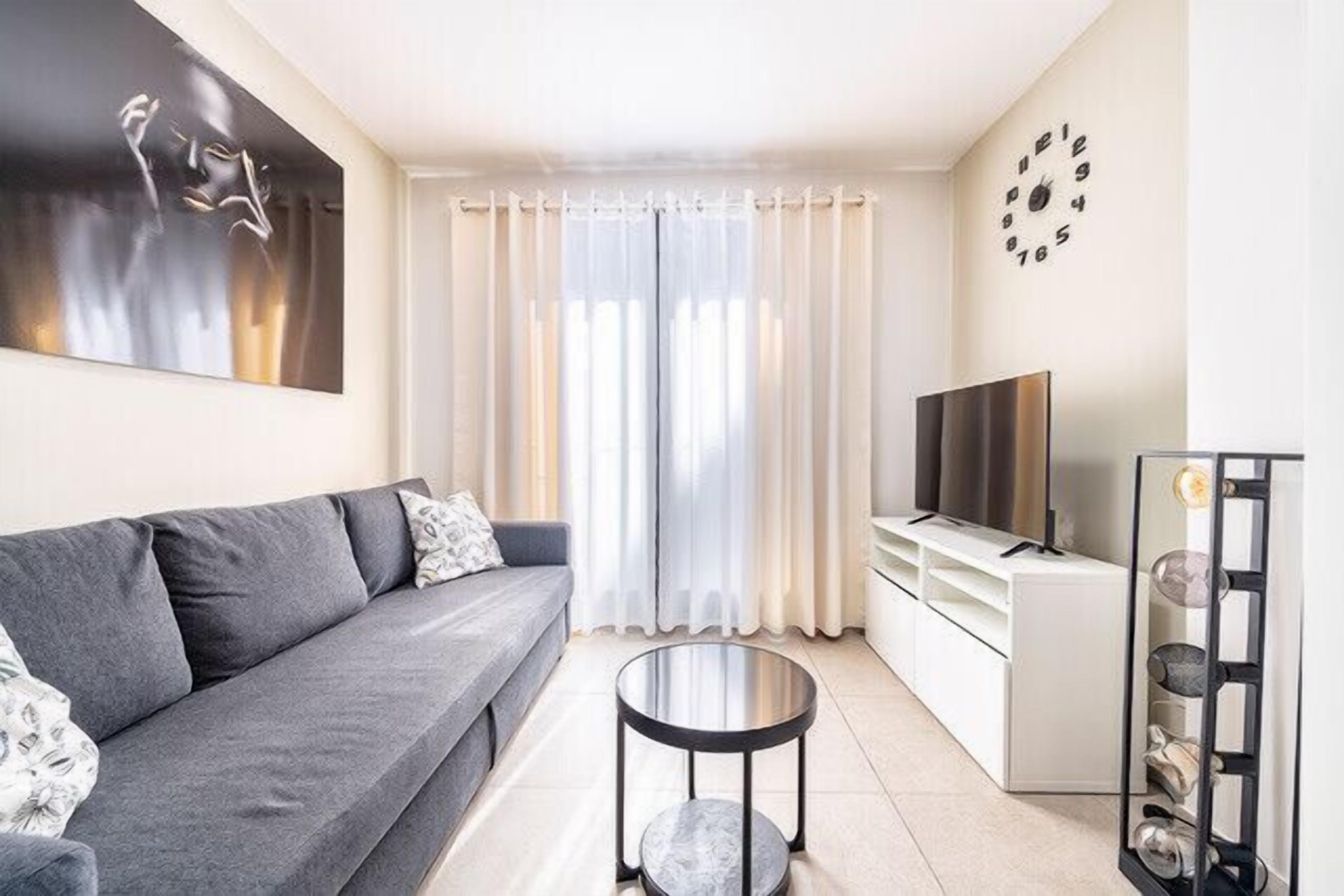 Una sala de estar moderna con un sofá gris, una mesita redonda pequeña, un televisor y un adorno de pared.