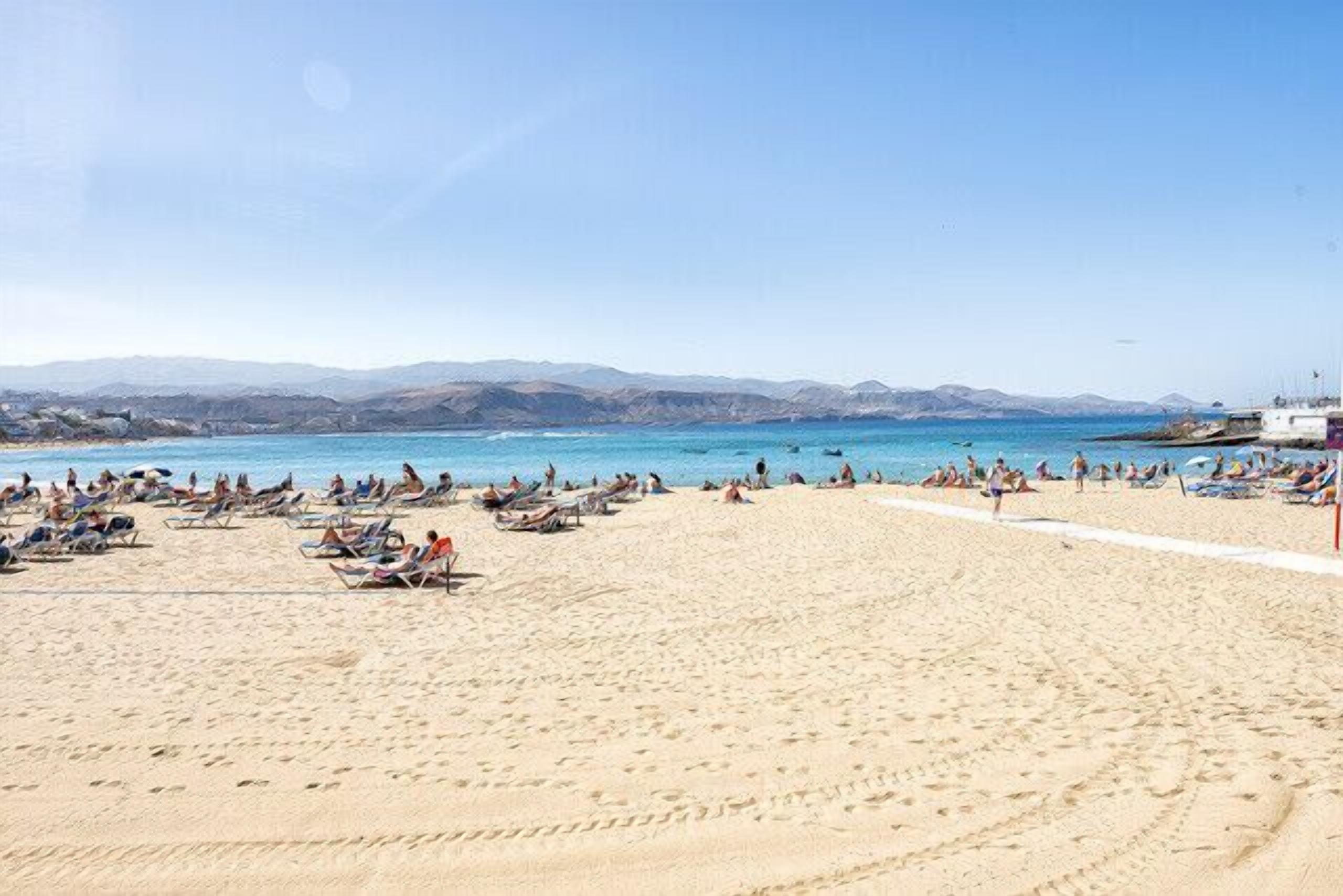 A beach with people, sun loungers, and a clear sky.