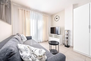 Een moderne woonkamer met een grijze bank, een televisie, een bijzettafeltje en een kledingkast.
