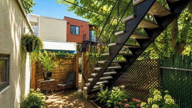 Et moderne udendørsareal med træterrasse, metal trappe og mange planter.