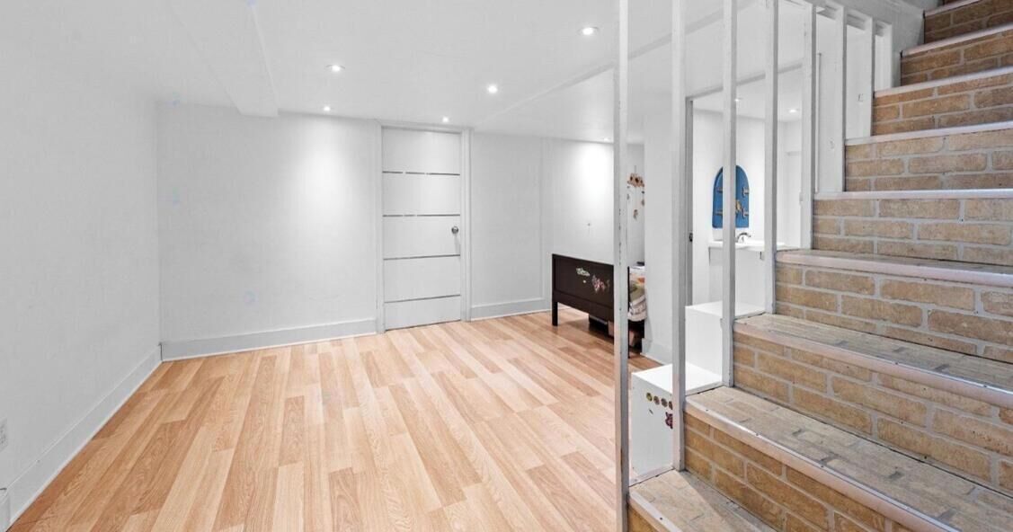 A room with a wooden floor, a staircase with brick steps, and a white door.