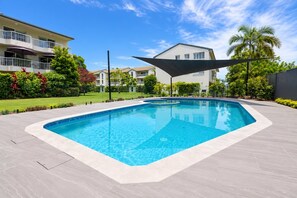 A swimming pool with a surrounding patio area, a building with balconies, and a palm tree. - The Burleigh Hideaway (Gold Coast)