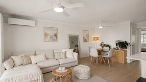 Un salon moderne avec un canapé, un coin repas comprenant des chaises et une table, et un ventilateur de plafond.