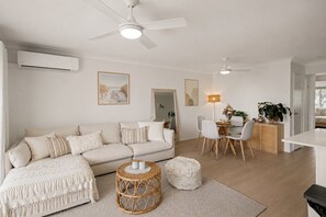 Ein modernes Wohnzimmer mit einer Couch, einem Essbereich mit Stühlen und einem Tisch sowie einem Deckenventilator.