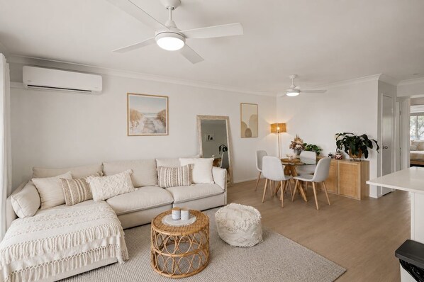 Uma sala de estar moderna com um sofá, um espaço de refeições com cadeiras e uma mesa, e um ventilador de teto.