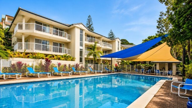 Une piscine avec des chaises longues et un bâtiment doté de balcons.