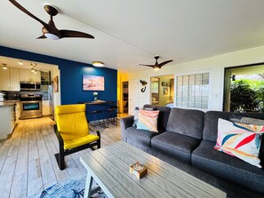 Ein modernes Wohnzimmer mit einer Couch, einem gelben Sessel, einem Couchtisch und einer Küche im Hintergrund.