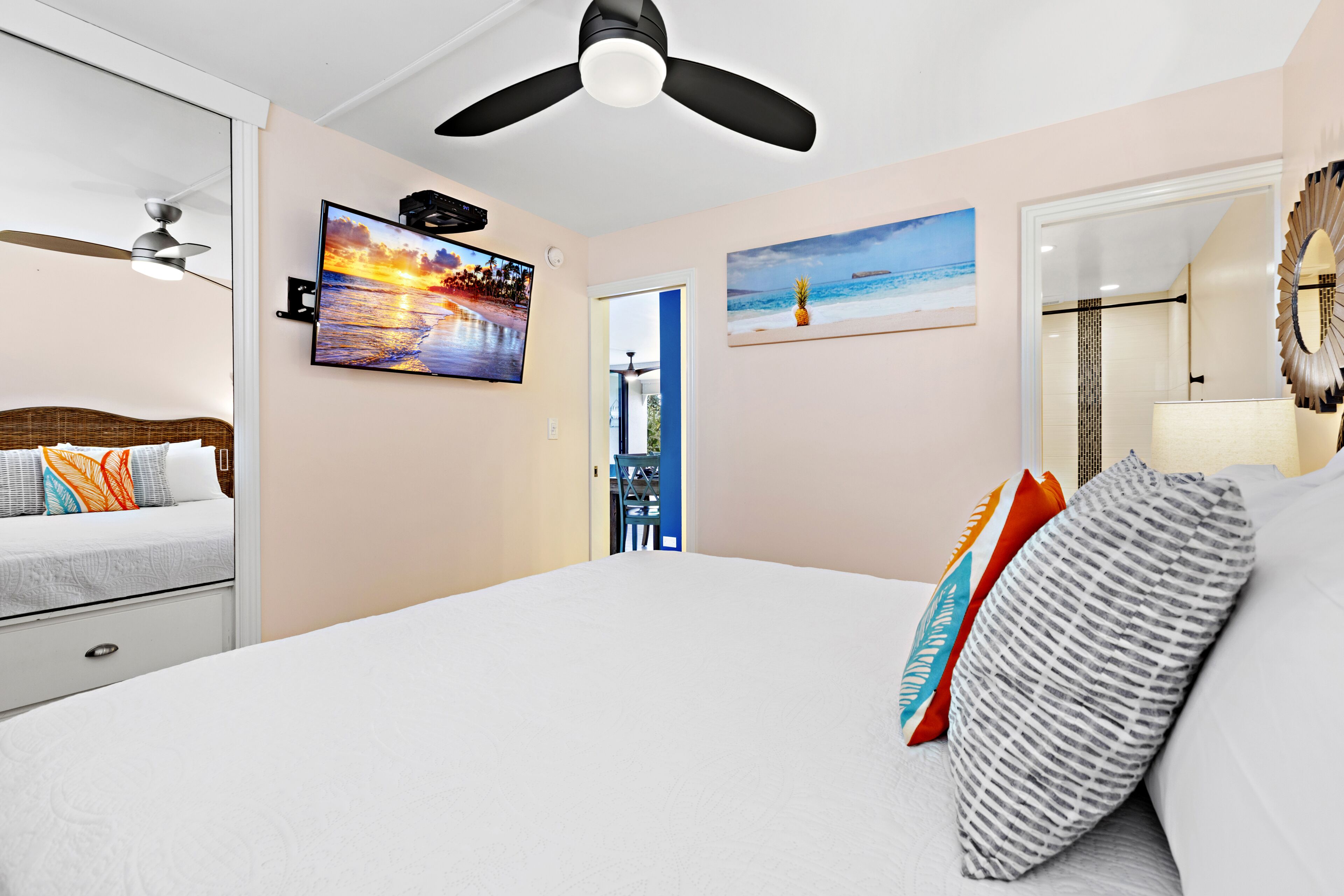 A bedroom with a bed, a ceiling fan, a TV, and artwork on the walls.