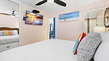 A bedroom with a bed, a ceiling fan, a TV, and artwork on the walls.