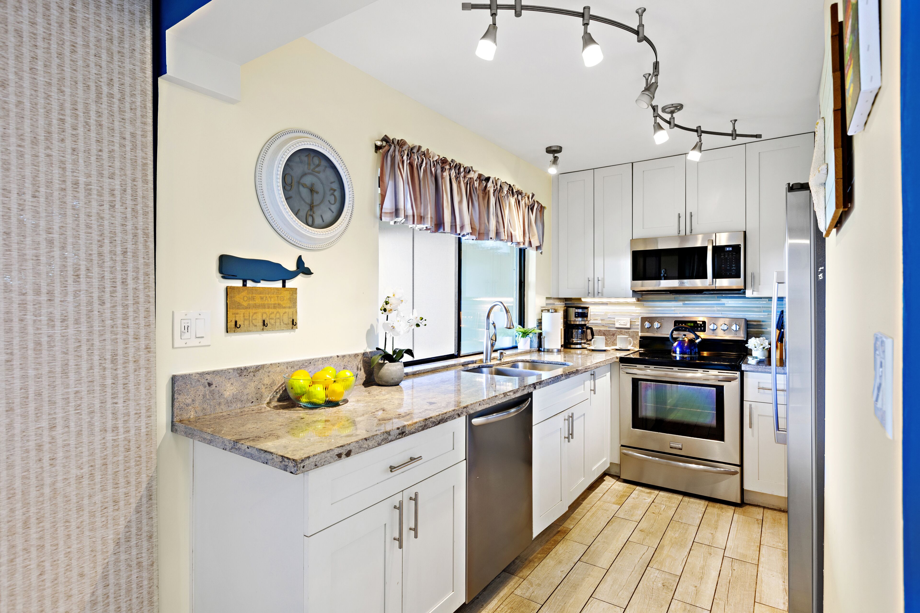 A modern kitchen with white cabinets, stainless steel appliances, a dishwasher, and a clock on the wall.