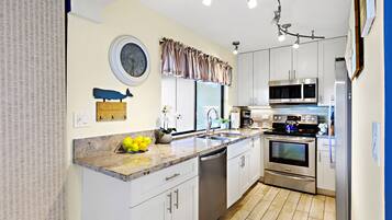 A modern kitchen with white cabinets, stainless steel appliances, a dishwasher, and a clock on the wall.