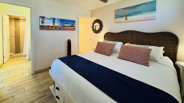 Una camera da letto con un letto, una ventola a soffitto, un quadro e una porta che conduce al bagno.